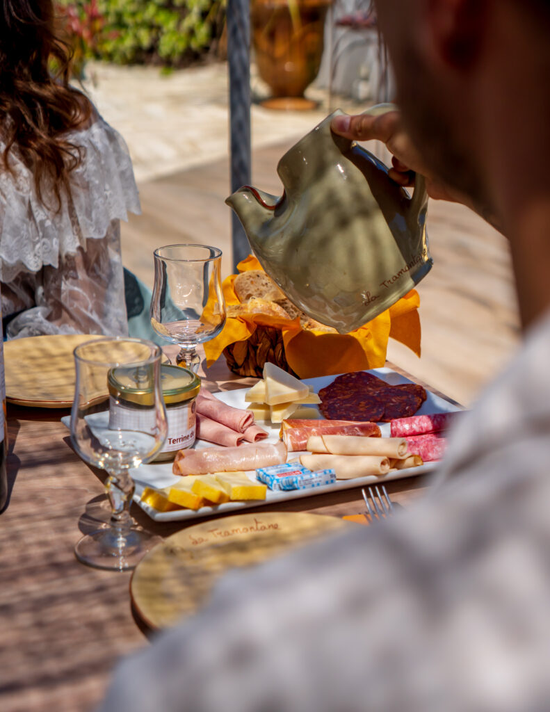 Table sur la terrasse avec planche de charcuterie et panier de pain, un garçon servant une carafe d’eau à une fille assise en face