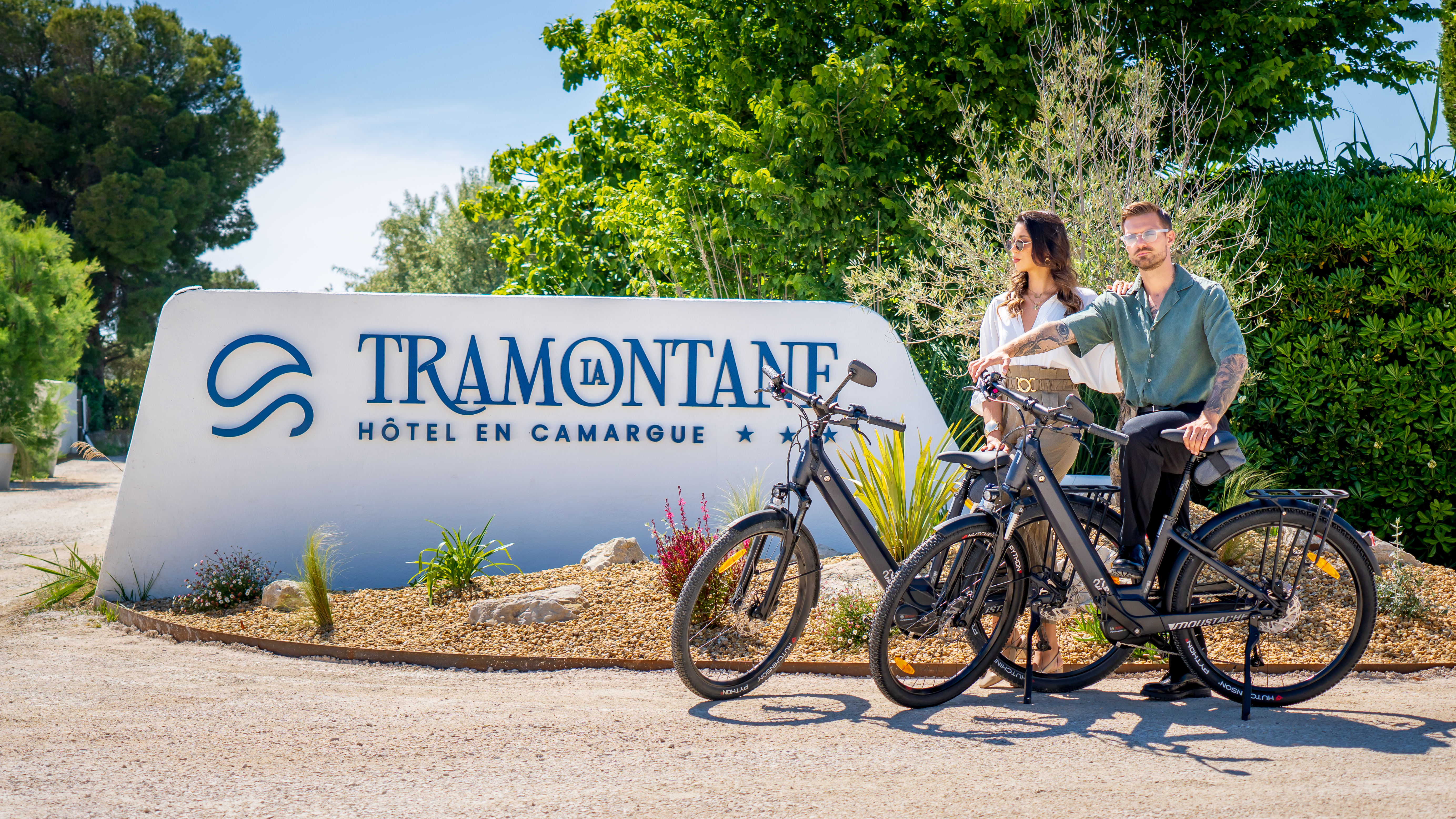 Une fille et un garçon posent sur un vélo électrique devant l’enseigne de l’hôtel sous un jour ensoleillé