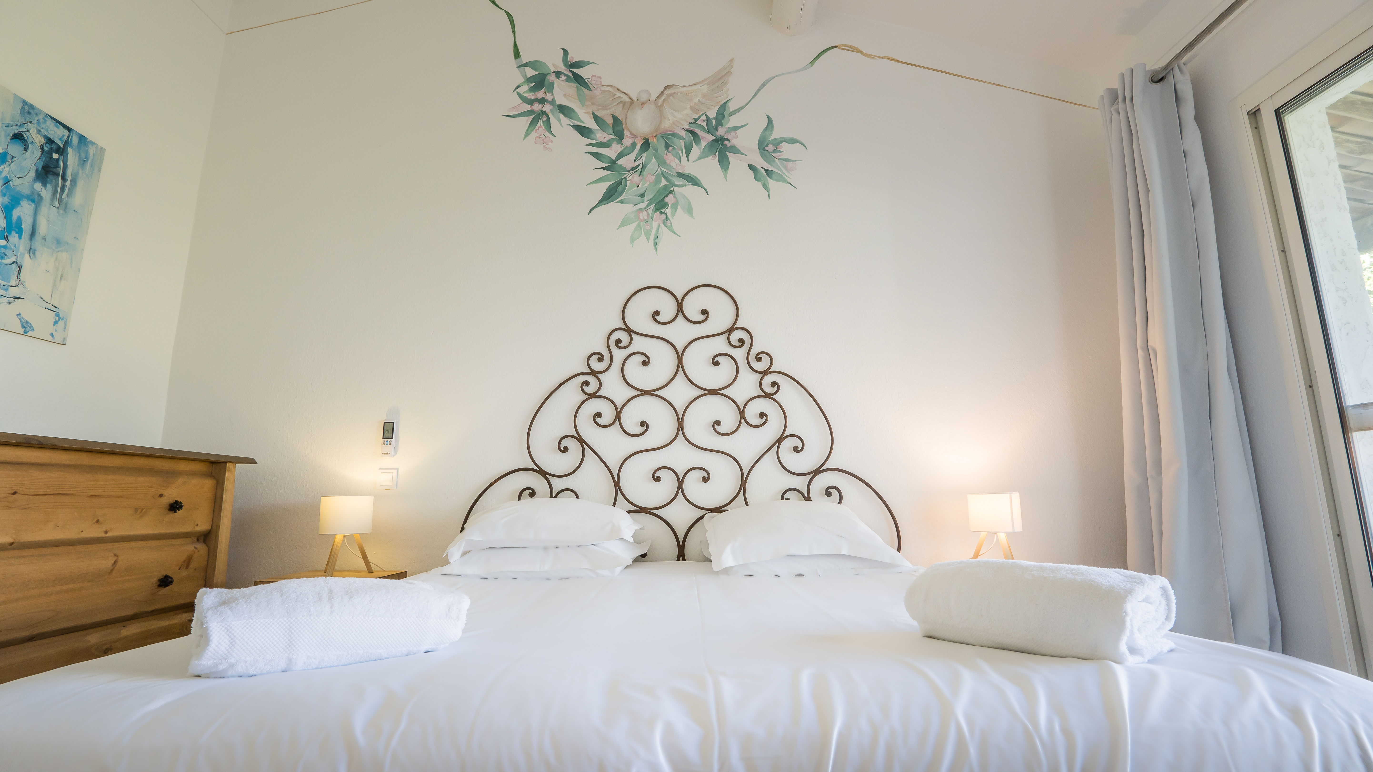 Lit bien présenté avec tête de lit en fer décorative, peinture d’oiseaux au-dessus, lampes de chevet allumées